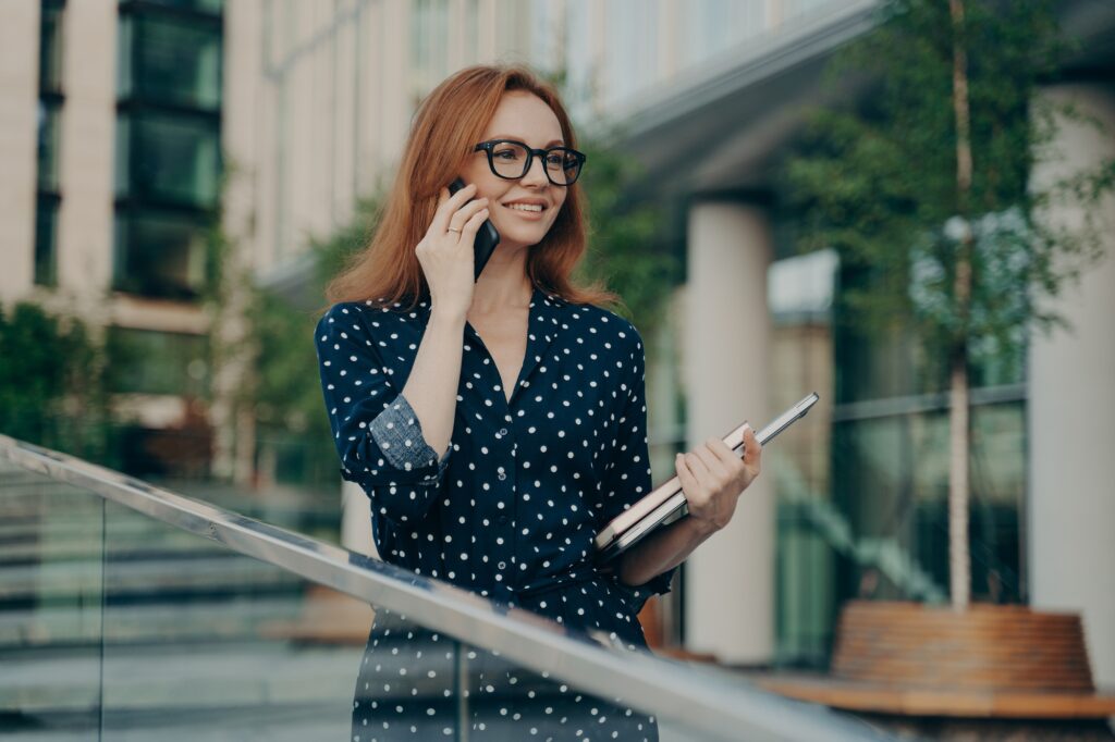 Happy adult lady with red hair makes consultancy call on smartphone